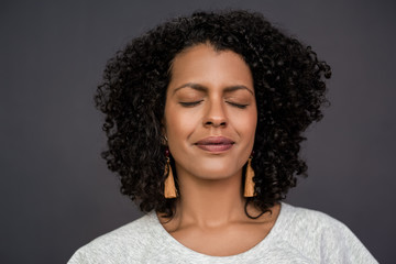 Content young woman standing with her eyes closed on gray