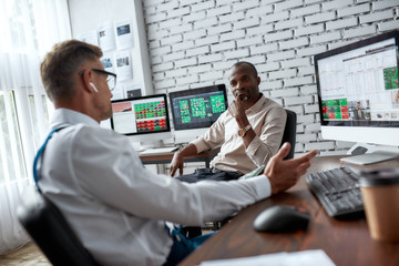 Ensuring Finacial Freedom. Two diverse colleagues traders talking to each other while sitting in...