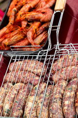 raw sausages and langoustines into grill grate on the red table are ready to be grilled