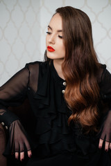 Portrait of beautiful elegant woman in black dress sitting on armchair. Pensive look down.