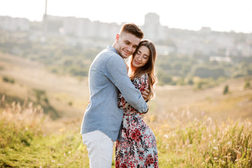 Young couple is hugging and walking in summer field with grass on the background town. Man and woman. Concept of lovely family.