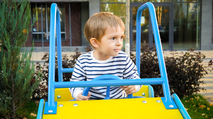 Happy smiling boy riding in big toy car on children playground