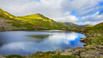 Fototapeta na wymiar small lake in a green mountain valley, mountain ridge and cloudy sky natural background
