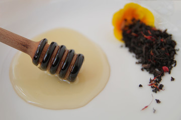 
honey dipper with liquid honey, on the background of dry tea leaves, on a white plate.