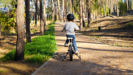 Little boy in helmet riding bicycle up the hill at park