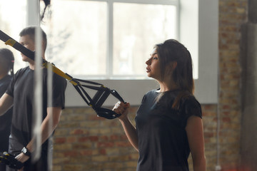 Continue doing it. Athletic young woman doing fitness TRX training exercises at industrial gym....