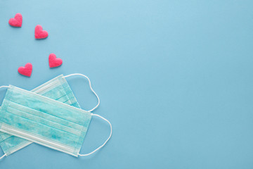 medical surgical protective ear-loop masks and red hearts on pastel blue background, top view, flat lay, protection concept, copy space