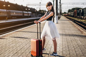 Female brunette traveler with red suitcase walking on raiway station