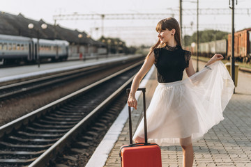 Female brunette traveler with red suitcase walking on raiway station