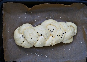 Homemade challah prepared for baking, white wicker bread sprinkled with white and black sesame seeds on baking paper.