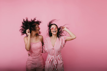 Trendy young women dancing in studio. Portrait of two female friends laughing while jumping together