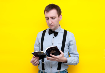 handsome confident man in blue shirt and suspender reading usa constitution and independence declaration on yellow background with copy space