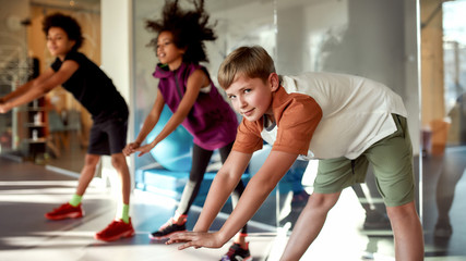 Exercise your body. Portrait of a boy looking at camera while warming up, exercising together with other kids in gym. Sport, healthy lifestyle, active childhood concept