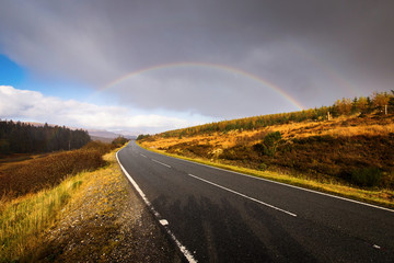Autumn landscape in Highlands, Scotland, United Kingdom. Road with beautiful and colourful rainbow in background.