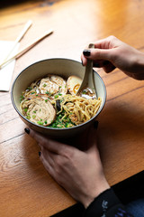 Vertical frame - woman hand holding a Japanese ceramic spoon and scoops a pack of noodles from a...