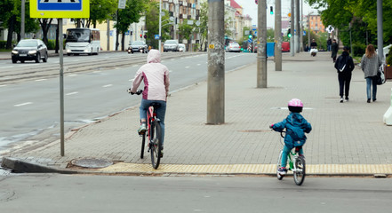 A child in a bicycle helmet with his mom on bicycles rides on the sidewalk
