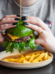Big delicious meat Burger with two beef patties. With French fries.Green rolls. Cheese and green salad. The girl is holding a Burger in her hands. Menu for cafes and restaurants. Children's Burger.