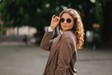 Portrait of attractive woman with curly hair in sunglasses outdoors. Happy young woman walking in the city