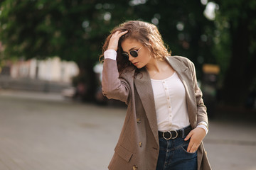 Portrait of attractive woman with curly hair in sunglasses outdoors. Happy young woman walking in the city