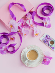 Obraz na płótnie Canvas Delicate flatlay composition with morning cup of coffee with milk or cappuccino, letters, pink gift bag and orchid flowers on light pink background.