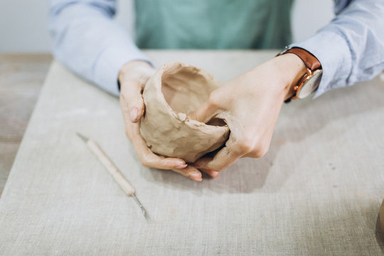 The potter's hands are shaped a cup from a clay. The process of creating pottery. The master ceramist works in his studio. Close-up, only hands. Crockery from clay own hands.	