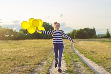 Happy teenager girl with balloons running and jumping along country road