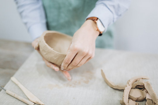 The potter's hands are shaped a cup from a clay. The process of creating pottery. The master ceramist works in his studio. Close-up, only hands. Crockery from clay own hands.	