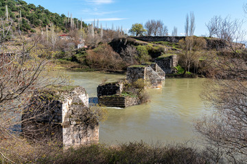 Fototapeta na wymiar Ruined ancient bridge in green river. Ancient settlement in Anatolia