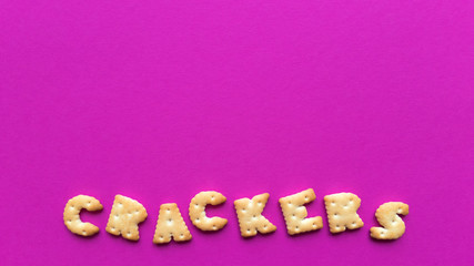 Crackers word on pink background. Simple flat lay with pastel texture and copy space. Stock photo.