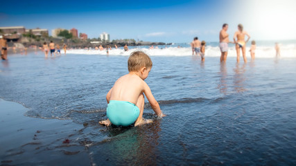 Cute little boy sitting on the ocean beach and waiting for the sea wave