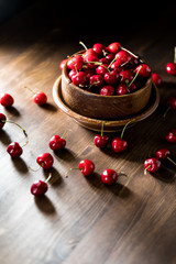 A vertical close up view of a bowl filled with sweet cherries against a dark background.