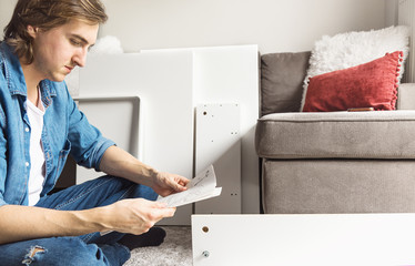 Concentrated young man reading the instructions to assemble furniture at home in the living room