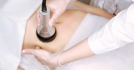 The cavitation procedure closeup. Beautician apparatus for cavitation on the woman's stomach. The...