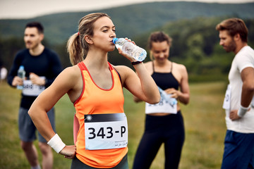 Thirsty athletic woman drinking water after running a marathon in nature.