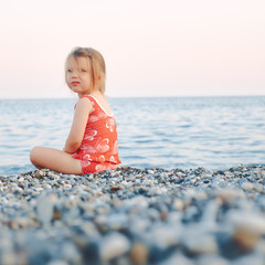 girl child sitting on a rocky shore on a background of the sea