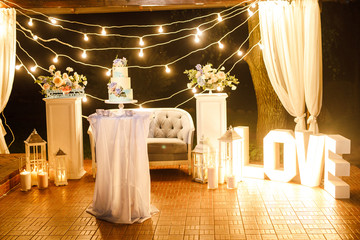 night wedding ceremony, the arch is decorated with flowers, candles and garlands of light bulbs and there is a wedding cake on the table