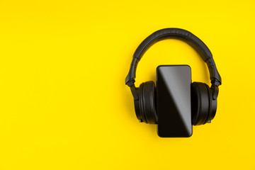 Black wireless headphones and smartpnone on abstract yellow colorful background with copy space