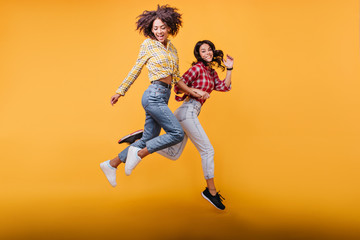 Fototapeta na wymiar Young women with curly hair run on orange background. Models in streetwear posing in jump