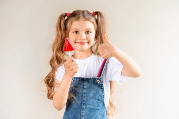 A little girl holds a Lollipop in her hand and gives a thumbs up.