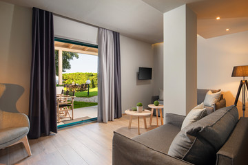 Modern gray and wooden living room with big French window and green garden terrace. Eco style interior concept design