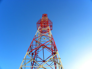 Red and white telecommunications tower and satellite dish of a telecom network against a blue sky  ...
