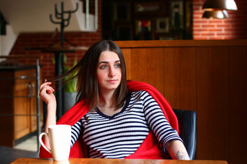 Pensive woman is sitting at the table in a restaurant, straightening her hair and looking to the window