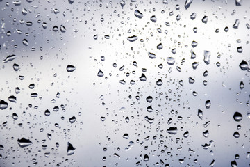 Drops of morning summer rain on the transparent window of the house on a blurred background of nature. Summer vacation and travel concept