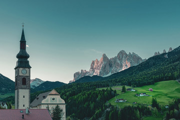 Beautiful view of church in Italian village San Pietro in Dolomites Alps at sunrise. Val di Funes,...