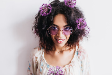 Studio portrait of charming black girl posing with allium. Indoor photo of pretty african female model holding purple flowers and smiling.