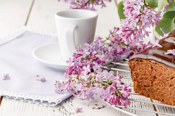 Brownie, watered with chocolate on a wooden background with a bouquet of lilacs