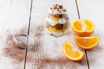 creamy trifle in beautiful glasses and cut fresh ripe fruit on white wooden background - healthy eating concept