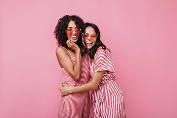 Cousins in dark curly hair in great mood posing for portrait. Girls in pink outfits have fun