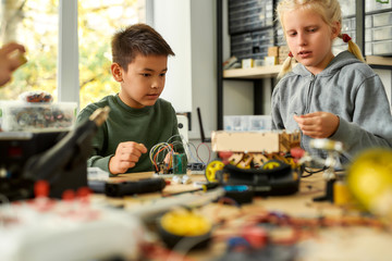Young generation. Asian boy and caucasian girl making their own vehicles at a stem robotics class. Inventions and creativity for children.
