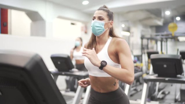 Woman with face mask running on electrical treadmill in gym.